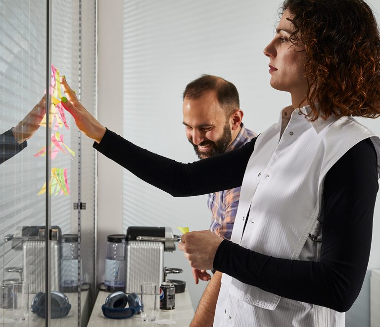 Two colleagues arranging sticky notes on a glass wall