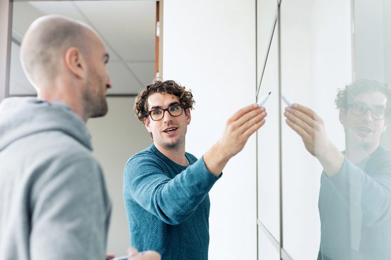 Two engineers working through a problem at a whiteboard