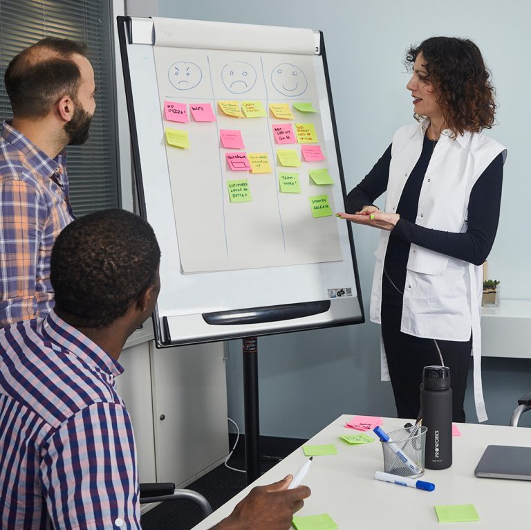 A trainer leading a session at a whiteboard covered in sticky notes